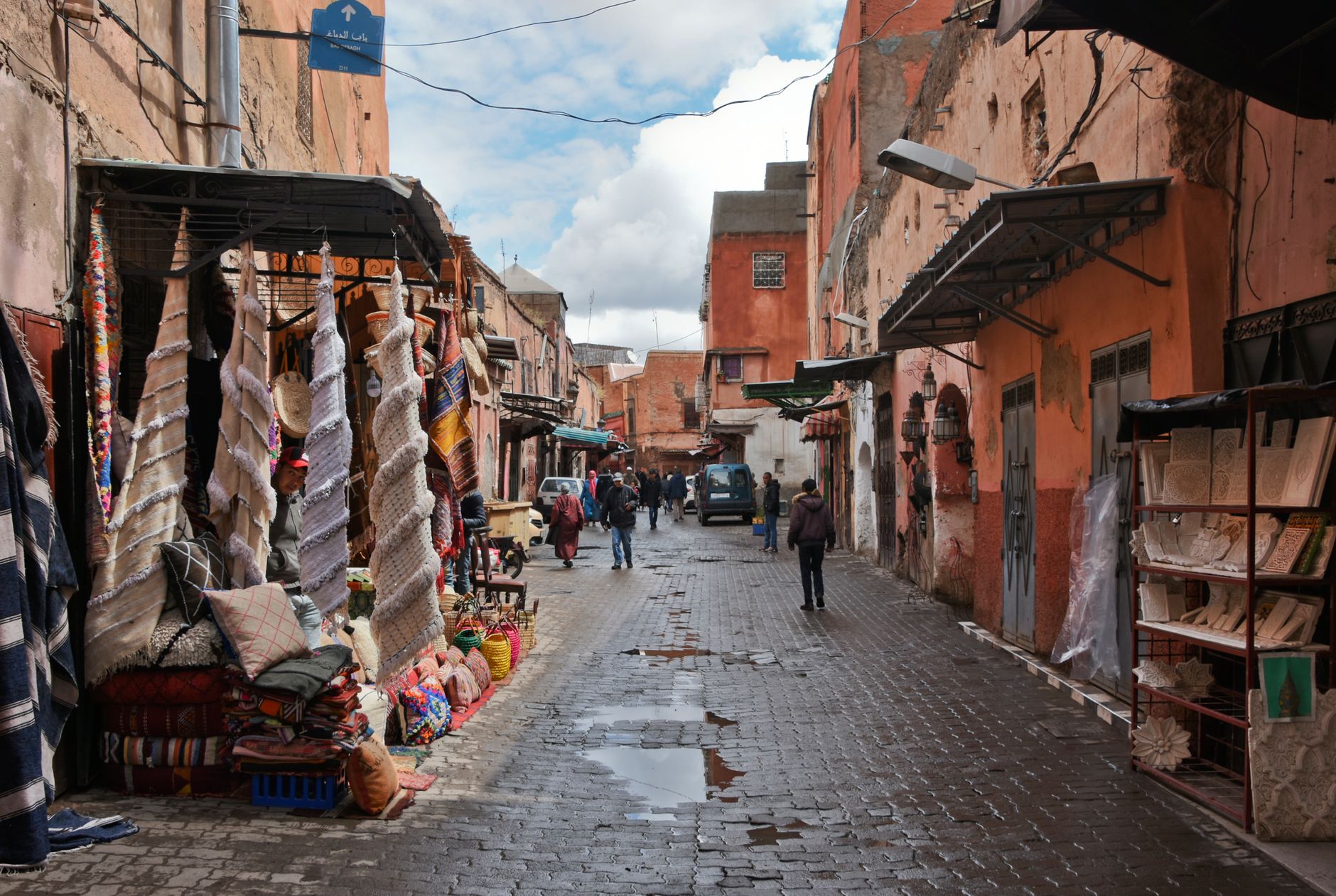 ruelle animée de la médina de Marrakech avec échoppes de tapis et de coussins, au Maroc